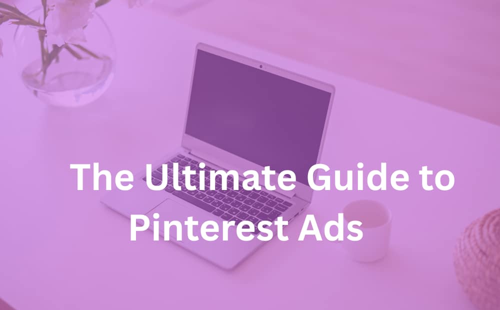 Laptop on pink-tinted desk with text "The Ultimate Guide to Pinterest Ads." Vase of flowers and coffee cup in background, conveying a modern and creative tone.